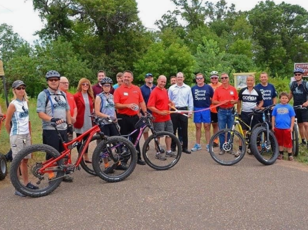 Chippewa Falls Chamber of Commerce Ribbon cutting - a gruop of people gathered at a trailhead cutting a ribbon
