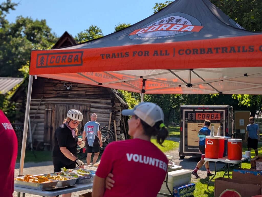 volunteer standing under a tent with rider taking food set out