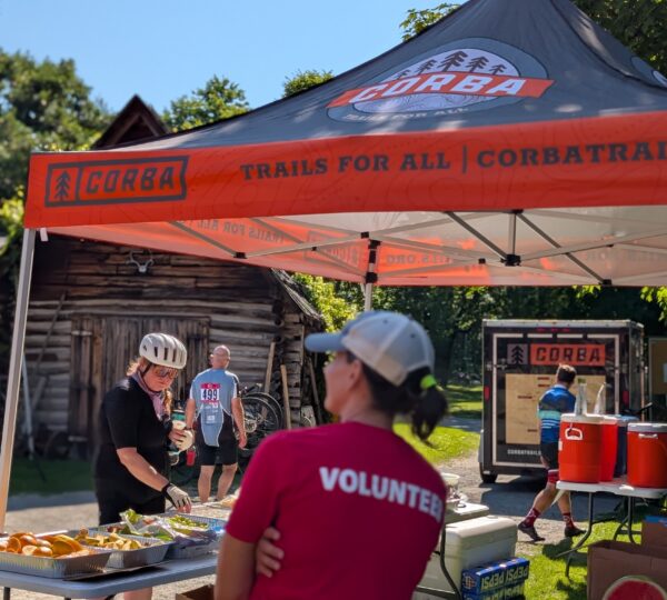 volunteer standing under a tent with rider taking food set out